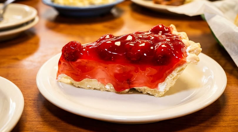 A slice of cherry pie with a thick, glossy red topping on a white plate.