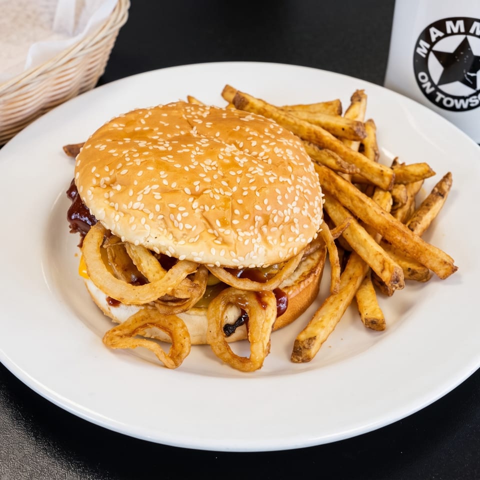 A burger with onion rings and fries on a white plate, with a "Mamma's on Towson" mug.