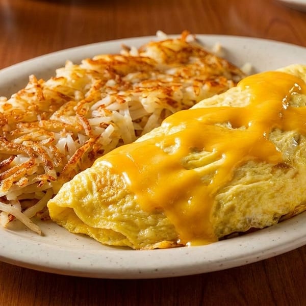 A cheesy omelet and crispy hash browns are served on a white plate on a wooden table.